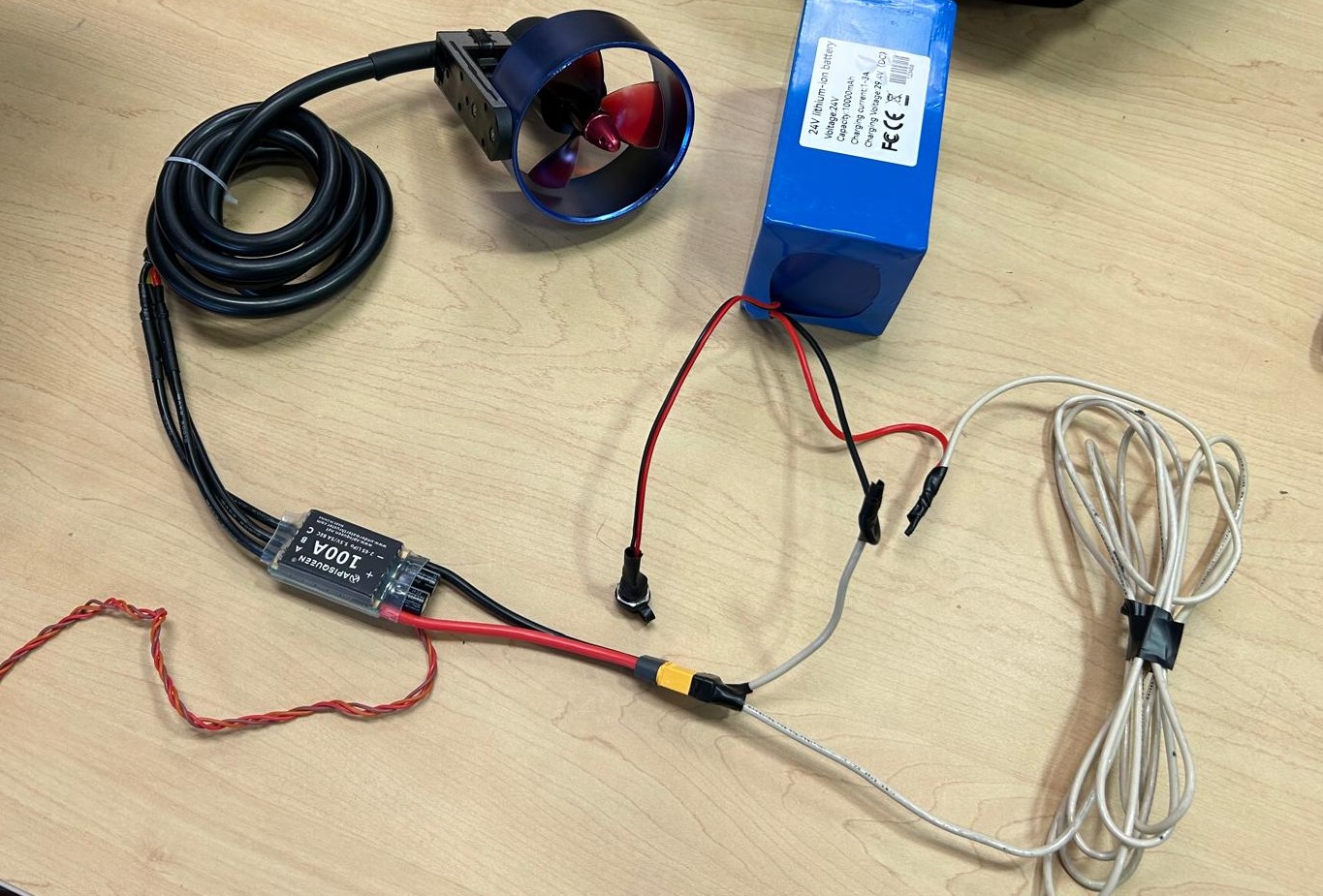 Blue/red thruster, APISQUEEN ESC and labeled battery with loose leads on a workbench.